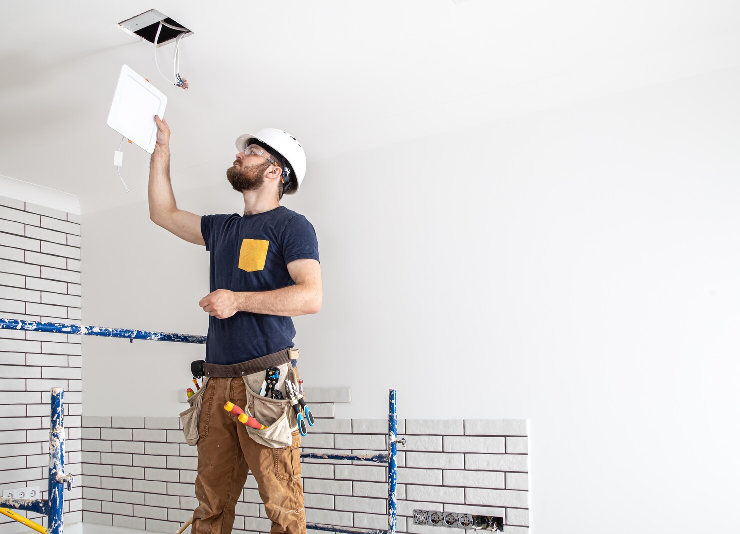electrician builder with beard worker white helmet work installation lamps height professional overalls with drill background repair site 169016 7327